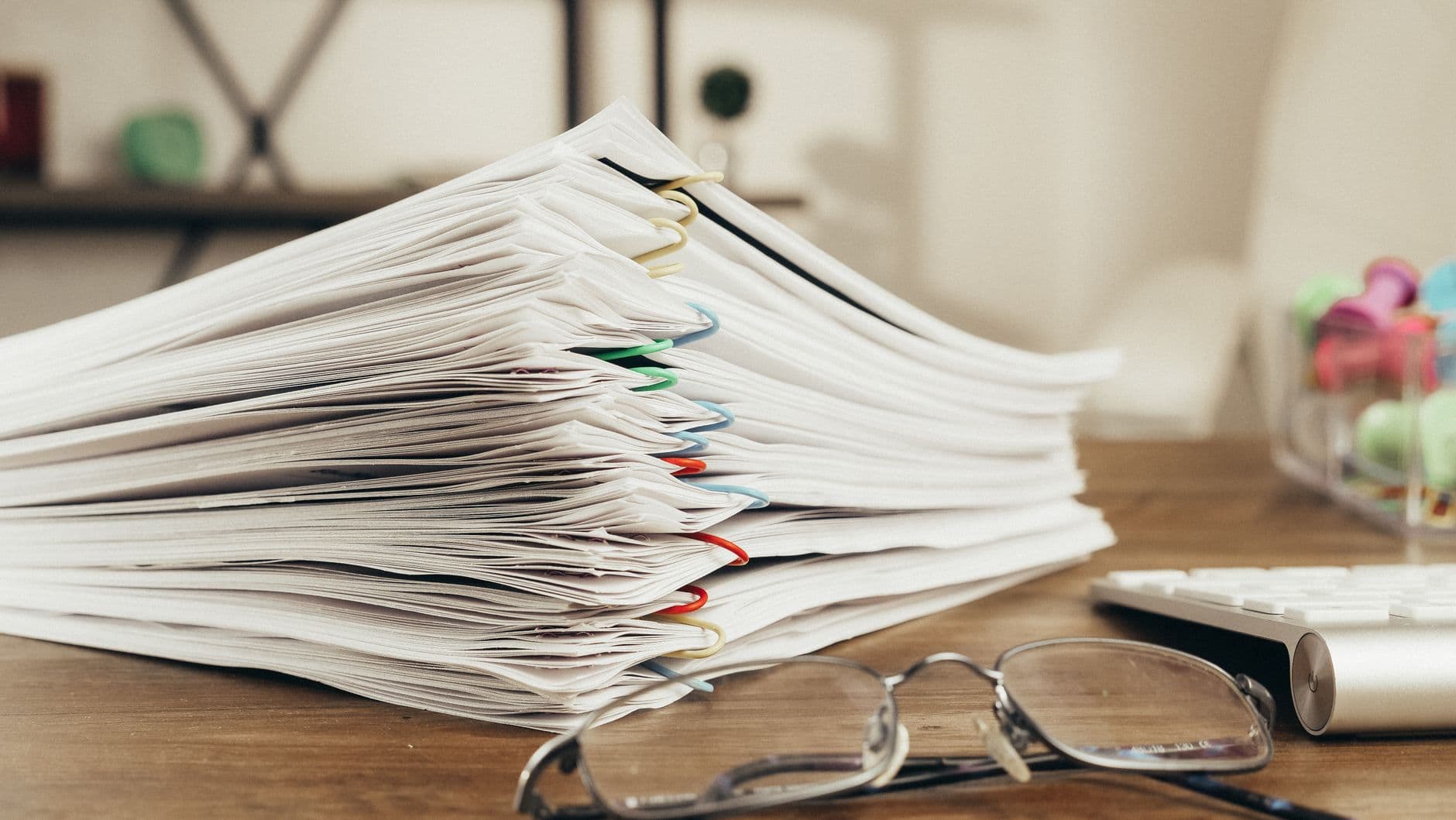 Une pile de dossiers agrafés, des lunettes et un clavier sur un bureau en fin de journée