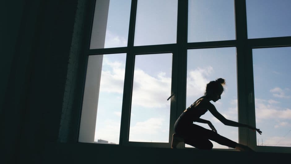 Silhouette en posture de yoga à contre-jour devant une grande fenêtre